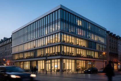 Façade vitrée d'un immeuble de bureaux européen en fin de journée, lumière intérieure visible.