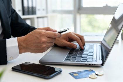 Mains d'un professionnel réglant un paiement sur ordinateur portable et smartphone, carte bancaire posée sur un bureau