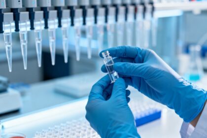 Mains gantées de bleu tenant un petit flacon transparent dans un laboratoire de biotechnologie