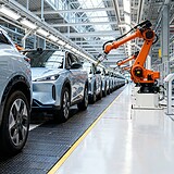 Rangée de SUV électriques neufs sur une chaîne d'assemblage et bras robotisé orange dans une usine automobile