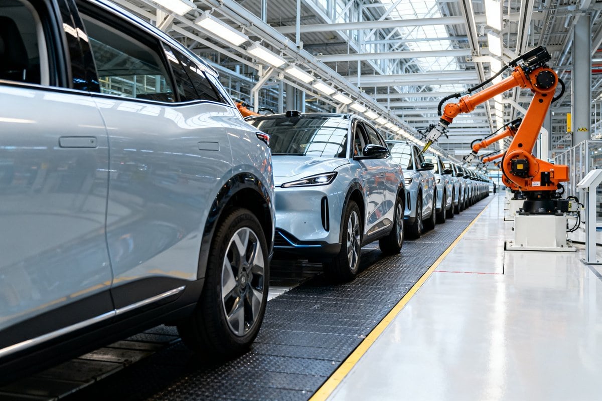 Rangée de SUV électriques neufs sur une chaîne d'assemblage et bras robotisé orange dans une usine automobile