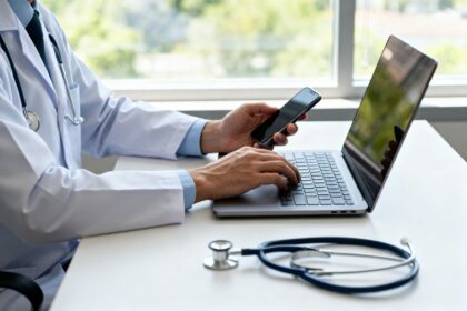 Mains d'un médecin utilisant un ordinateur portable et un smartphone sur un bureau, stéthoscope à côté