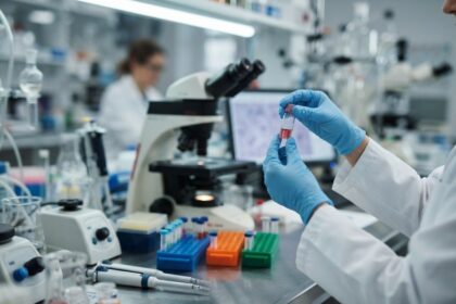 Mains gantées tenant un flacon d'échantillon près d'un microscope dans un laboratoire de recherche biomédicale.