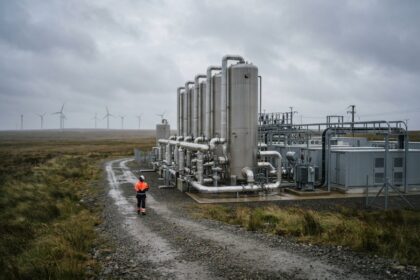 Cuves métalliques et conteneurs d'un site de stockage d'électricité, un technicien en gilet orange, éoliennes au loin