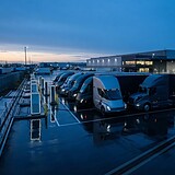 Rangée de camions électriques branchés à des bornes de recharge sur le parking d'un dépôt logistique au crépuscule
