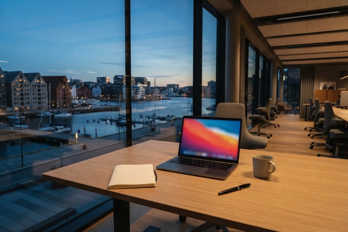 Ordinateur portable ouvert sur un bureau en bois clair face à une baie vitrée donnant sur un port nordique au crépuscule