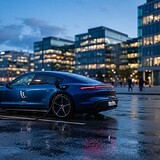 Berline sportive bleue branchée à une borne de recharge électrique au crépuscule, immeubles de bureaux en arrière-plan