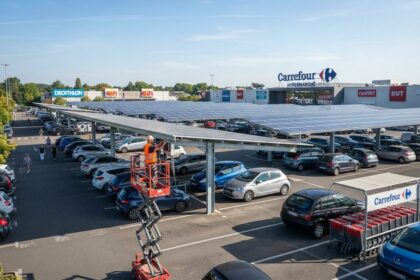 Parking de zone commerciale équipé d'ombrières photovoltaïques, technicien sur nacelle devant un hypermarché