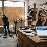 Commerçante devant un ordinateur affichant une demande d'activité partielle, vitrine condamnée par des panneaux de bois
