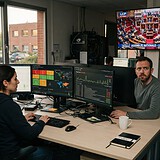 Deux analystes en cybersécurité devant leurs écrans, une télévision diffuse une séance de l'Assemblée nationale